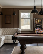 Farmhouse game room with a dark wood billiard table, a cream linen Chesterfield sofa, matte black metal lighting fixtures, and a vintage pinball machine against a wall painted in 'Swiss Coffee'. — alternate angle