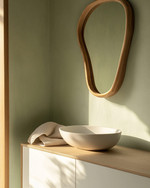 A serene Japandi powder room featuring a floating white oak vanity with a matte white vessel sink, an organically shaped mirror with a slim natural wood frame, and a soft sage green limewash wall. — alternate angle