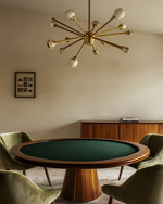 A mid-century modern game room featuring a walnut poker table with a dark green felt top, surrounded by olive velvet low-slung armchairs, illuminated by a brass Sputnik chandelier, with a teak credenza against a soft ivory wall. — styling and décor detail