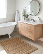 A vintage modern coastal bathroom featuring a white clawfoot tub, a light oak floating vanity, and a round frameless mirror, accented with polished nickel fixtures and a jute bath mat.