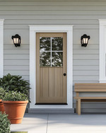 A serene Scandinavian exterior with a light gray facade, crisp white trim, and a natural wood front door. Simple black sconces flank the door, and a minimalist wooden bench sits beside terracotta planters filled with green foliage, all under a bright, clear sky. — styling and décor detail