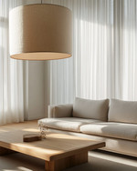 A Japandi family room showcasing a large, linen-shaded drum pendant light, a low-profile light grey sofa, and a minimalist oak coffee table, with soft daylight filtering through sheer curtains.