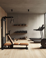 A clean rustic home gym featuring light reclaimed wood flooring, a smooth concrete accent wall, a simple black wrought iron shelf, and minimalist workout equipment with wooden and leather details, bathed in soft ambient lighting. — styling and décor detail