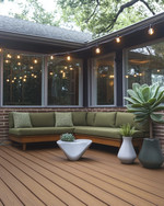 A budget-friendly Mid-Century Modern deck featuring stained pine decking, a low-slung sofa with olive green cushions, and a kidney-shaped side table. Fiberglass planters hold architectural succulents and a large fiddle-leaf fig, all under string lights with exposed bulbs. — alternate angle