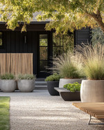 A Scandinavian front yard featuring a pea gravel path, large concrete planters with ornamental grasses, a low woven willow fence, and a slatted wooden bench by the matte black front door. — alternate angle