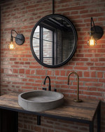 Industrial powder room featuring a wall of exposed red brick, a reclaimed wood vanity with a concrete sink basin, and a round black metal mirror. Dark iron sconces with exposed Edison bulbs illuminate the space, and a patinated brass faucet adds warmth. — styling and décor detail