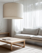 A Japandi family room showcasing a large, linen-shaded drum pendant light, a low-profile light grey sofa, and a minimalist oak coffee table, with soft daylight filtering through sheer curtains. — styling and décor detail