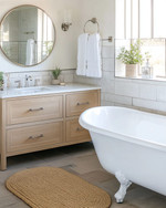 A vintage modern coastal bathroom featuring a white clawfoot tub, a light oak floating vanity, and a round frameless mirror, accented with polished nickel fixtures and a jute bath mat. — close-up of textures and materials