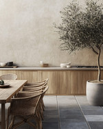 Japandi outdoor kitchen featuring untreated teak cabinetry, honed concrete countertops, and bluestone pavers. Minimalist rattan dining chairs surround a solid wood table, with an olive tree in an unglazed ceramic planter providing a natural accent. — styling and décor detail