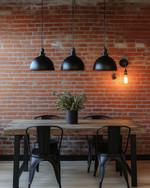 Industrial breakfast nook featuring a reclaimed wood table, black metal chairs, and three matte black dome pendant lights hanging low. An exposed red brick wall provides a textured backdrop, and an exposed Edison bulb sconce adds warm, ambient lighting. — alternate angle