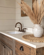 A cozy rustic powder room featuring a reclaimed wood vanity with an off-white quartz countertop, an oil-rubbed bronze faucet, and shiplap walls painted in a soft greige. A woven jute rug sits on the floor, and a ceramic vase with dried pampas grass adorns the counter.