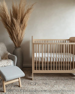 A serene Japandi baby room with a light wood crib, a soft grey glider, and a neutral rug, accented by a tall dried pampas grass arrangement in a ceramic vase and a subtly patterned throw blanket. — alternate angle