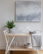 A serene Scandinavian home bar setup in a rental apartment featuring a light wood bar cart with white metal accents, minimalist glassware, and a small potted fern. Soft grey wall art and a textured linen tea towel complete the inviting, renter-friendly space. — alternate angle