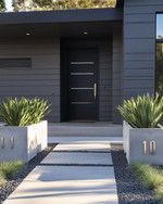 A modern exterior featuring a fresh coat of deep charcoal grey paint on the siding, a contrasting matte black front door, and sleek brushed nickel house numbers. The pathway combines light grey concrete pavers with dark pea gravel, and large concrete planters flank the entrance with sculptural green plants. — styling and décor detail