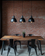 Industrial breakfast nook featuring a reclaimed wood table, black metal chairs, and three matte black dome pendant lights hanging low. An exposed red brick wall provides a textured backdrop, and an exposed Edison bulb sconce adds warm, ambient lighting. — close-up of textures and materials