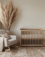A serene Japandi baby room with a light wood crib, a soft grey glider, and a neutral rug, accented by a tall dried pampas grass arrangement in a ceramic vase and a subtly patterned throw blanket. — close-up of textures and materials