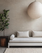 A serene Japandi poolhouse interior featuring a low-slung white oak daybed with natural linen cushions, a dark wenge wood side table, and a large, round paper lantern pendant light. The walls are a soft greige, complemented by a subtle textured rug in cream and a tall, slender fiddle leaf fig plant in a terracotta pot. — styling and décor detail