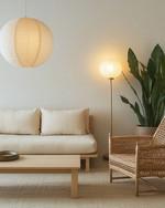A serene Japandi basement living area with a low-profile cream sofa, a light wood coffee table, and a woven rattan armchair. Warm diffused lighting comes from a paper lantern pendant and a minimalist floor lamp, while a large snake plant in a ceramic pot adds natural greenery. — alternate angle