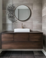 A modern powder room features a floating dark wood vanity with an integrated white quartz sink and brushed nickel faucet, set against large format charcoal grey porcelain tiles. A simple round mirror and abstract metal wall art complete the sleek, resilient design. — close-up of textures and materials