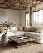 A cozy farmhouse poolhouse interior featuring a large cream sectional sofa with woven throw pillows, a distressed wood coffee table, and an exposed reclaimed wood ceiling. Soft light filters in, highlighting a natural fiber rug and a simple ceramic vase with greenery. — alternate angle