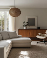 A Mid-Century Modern Craft living room featuring a walnut credenza, a low-slung sofa in natural linen, an Eames Lounge Chair, and a woven rattan pendant light, all bathed in warm, natural light. — close-up of textures and materials