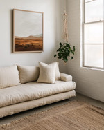 A small Boho Landscape living room featuring a low-slung sofa in natural linen, layered jute rugs, a minimalist abstract desert landscape print on the wall, and a trailing Pothos plant in a macrame hanger near a window. — styling and décor detail