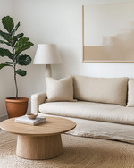 A serene Japandi great room featuring a low-slung oatmeal linen sofa, a light oak round coffee table, and a natural jute rug. Walls are painted in a soft off-white, adorned with a minimalist abstract nature print. A tall Fiddle Leaf Fig in a terracotta pot stands beside a ceramic table lamp with a linen shade, creating a calm and inviting atmosphere. — alternate angle
