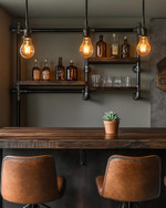 An inviting industrial home bar featuring a reclaimed wood countertop, dark metal pipe shelving, and leather bar stools. Warm Edison bulb pendants cast an amber glow, highlighting vintage amber glass bottles and a small potted succulent.