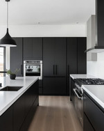 A sleek modern kitchen featuring matte black handleless cabinetry, white quartz countertops, integrated stainless steel appliances, and a minimalist black pendant light over a large kitchen island. — alternate angle