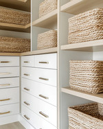 A clean coastal minimalist closet featuring light oak shelving, white built-in drawers with brushed nickel pulls, and tightly woven seagrass baskets, all bathed in natural light. — close-up of textures and materials