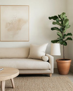 A serene Japandi great room featuring a low-slung oatmeal linen sofa, a light oak round coffee table, and a natural jute rug. Walls are painted in a soft off-white, adorned with a minimalist abstract nature print. A tall Fiddle Leaf Fig in a terracotta pot stands beside a ceramic table lamp with a linen shade, creating a calm and inviting atmosphere. — close-up of textures and materials