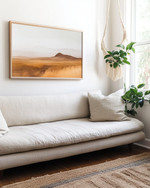 A small Boho Landscape living room featuring a low-slung sofa in natural linen, layered jute rugs, a minimalist abstract desert landscape print on the wall, and a trailing Pothos plant in a macrame hanger near a window. — alternate angle