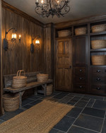 A rustic mudroom featuring warm layered lighting from a wrought iron chandelier and wall sconces, with slate floor tiles, a reclaimed wood bench, and dark wood storage cabinets, accented by woven baskets and a jute rug.