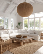 A bright coastal great room featuring a large off-white linen sofa, a reclaimed wood coffee table, and a natural jute area rug. Rattan armchairs flank the space, while a large woven pendant light hangs from the ceiling, all under ample natural light. — alternate angle
