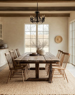 A rustic dining room featuring a large, solid reclaimed oak dining table, mismatched wooden chairs, and a natural jute area rug, illuminated by a wrought iron chandelier, with walls painted in a warm antique white. — close-up of textures and materials