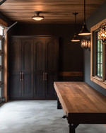 A traditional garage interior featuring a solid oak workbench, dark walnut storage cabinets with oil-rubbed bronze hardware, concrete flooring mimicking natural stone, and black iron industrial sconces. — alternate angle