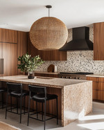 A Mid-Century Modern kitchen featuring flat-panel walnut cabinetry, a honed quartzite island, and a geometric terrazzo backsplash. A large woven rattan pendant light hangs above the island, which is flanked by black leather bar stools, all in soft natural daylight. — alternate angle