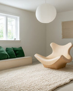 A bright Scandinavian basement living area featuring a light oak sculptural lounge chair, a large cream hand-knotted wool rug, and an oversized white paper lantern pendant light, with subtle forest green textile accents. — close-up of textures and materials