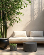 A small Japandi backyard featuring a low-profile teak bench with off-white cushions, a round grey stone side table, and a tall bamboo plant in a black ceramic planter, all set on light wood decking.