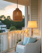 A well-lit coastal porch at dusk, featuring a woven rattan pendant light, string lights draped along the railing, and a floor lamp with a linen shade next to a white wicker chair with soft blue throw pillows. — close-up of textures and materials