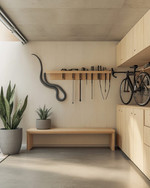 A small Japandi garage featuring light birch plywood cabinetry, a polished concrete floor, and walls painted in a soft off-white. A minimalist bamboo storage bench sits against one wall, with a single snake plant in a grey ceramic pot. Wall-mounted racks hold neatly organized tools, and a bicycle is suspended, maximizing floor space. — alternate angle