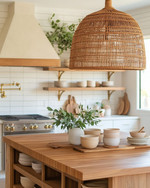 A bohemian kitchen featuring a large woven rattan pendant light above a wooden island with fresh greenery, open shelving with ceramic dishes, and warm brass fixtures creating a cozy, inviting ambiance. — styling and décor detail