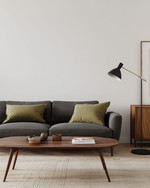 A minimalist Mid-Century Modern family room featuring a low-slung charcoal grey sofa, a walnut coffee table with clean lines, and an iconic Arco Floor Lamp, complemented by a muted olive green accent pillow and a simple credenza.