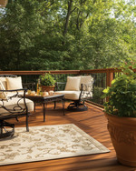 A traditional deck featuring warm-toned cedar decking and railings, wrought iron furniture with cream cushions, an outdoor rug in a natural beige, and terracotta planters filled with green foliage, all under soft, natural light.
