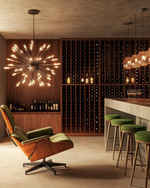 Mid-Century Modern wine cellar featuring a walnut Eames Lounge Chair, a Sputnik chandelier, sleek teak wine racks, and a concrete tasting bar with green upholstered stools.