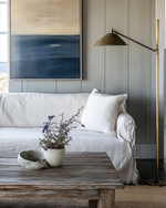 Coastal Landscape living room blending vintage and modern elements, featuring a reclaimed teak coffee table, a linen slipcover sofa, and a brushed brass floor lamp, with walls painted in a soft Balboa Mist grey and accents of deep ocean blue and coral. — alternate angle