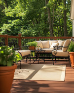 A traditional deck featuring warm-toned cedar decking and railings, wrought iron furniture with cream cushions, an outdoor rug in a natural beige, and terracotta planters filled with green foliage, all under soft, natural light. — alternate angle
