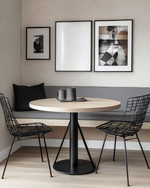 A modern breakfast nook features a light wood round table with a minimalist black metal base, paired with a charcoal grey upholstered bench and two black metal chairs. A subtle geometric peel-and-stick wallpaper adorns the wall, alongside a gallery of abstract art prints. — alternate angle