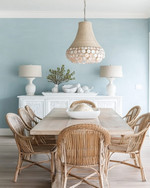 A coastal dining room featuring a light oak modern dining table, vintage rattan chairs, a distressed white buffet, and a contemporary capiz shell chandelier, with walls painted in a soft Palladian Blue. — close-up of textures and materials