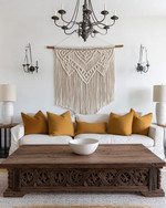 A Farmhouse Craft living room featuring a large, hand-carved reclaimed oak coffee table, a woven macrame wall hanging in ivory, and a wrought-iron chandelier, with ceramic table lamps and deep ochre throw pillows. — alternate angle